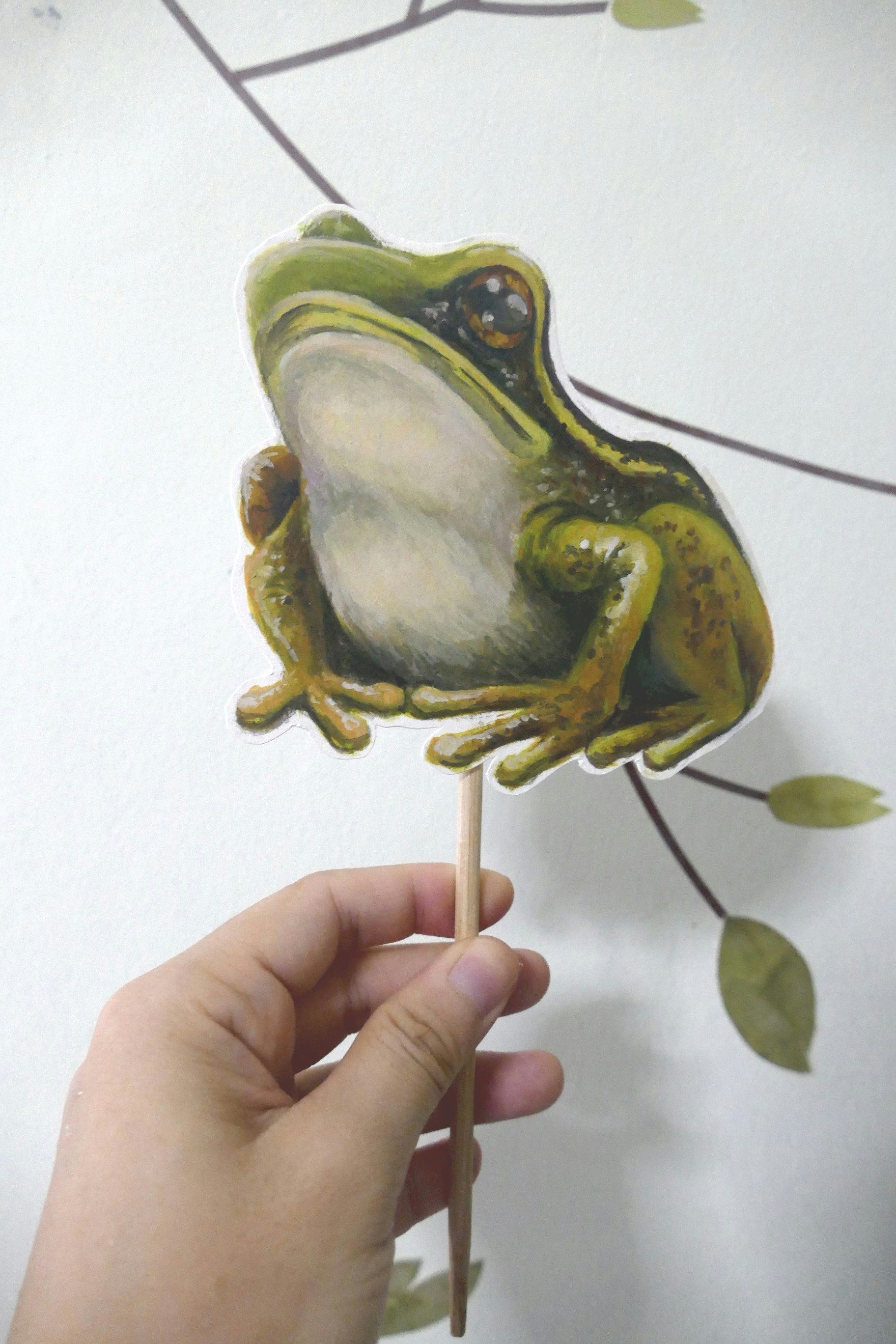 Poster painting cut-out on a stick of a common greenback frog, frontal three-quarter view in a resting pose