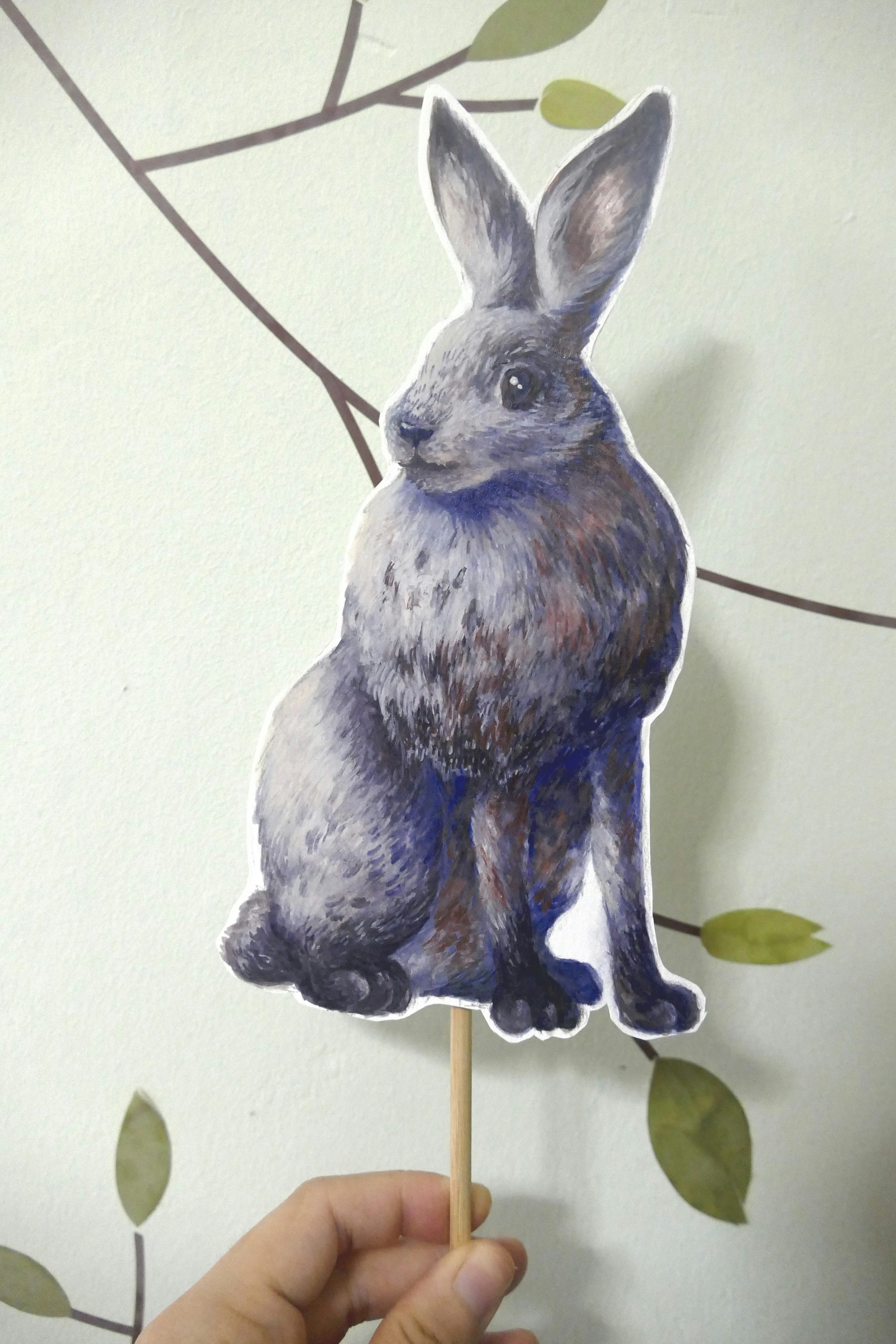 Poster painting cut-out on a stick of a white hare, sitting on its haunches and looking three-quarters left