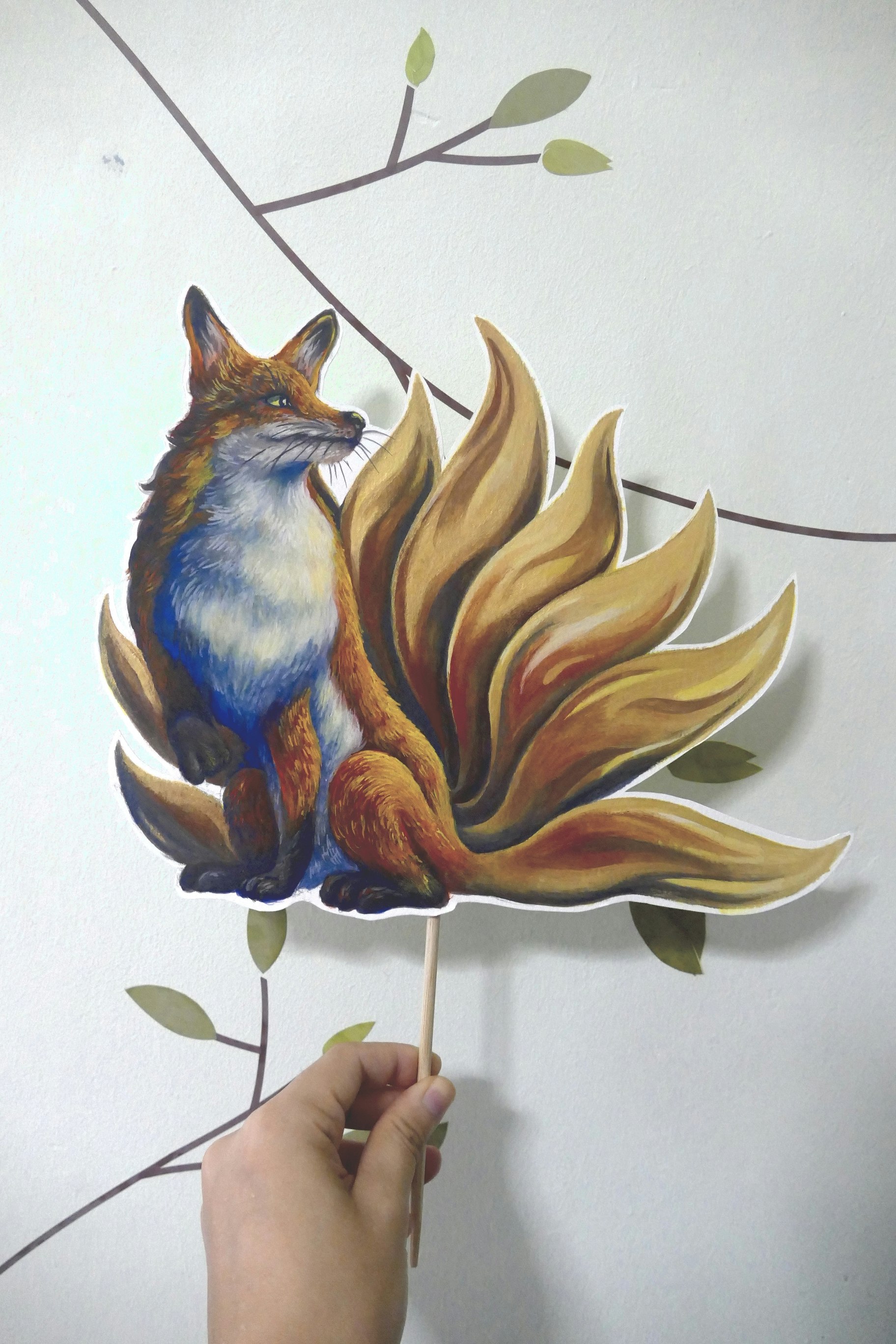 Poster painting cut-out on a stick of a red fox with nine-golden tails. The fox is looking admiringly at his tails